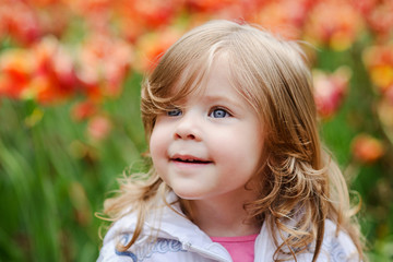 Fototapeta premium Cute curly hair blonde girl smiling with surprise on tulip bloss