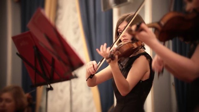 Chamber orchestra. A young woman playing violin during a musical performance.