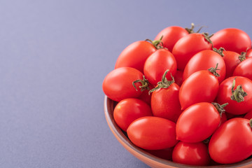 Fresh red cherry tomatoes in a wooden bowl isolated on a blue background, close up, copy space