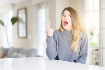 Obraz premium Young beautiful woman wearing winter sweater at home pointing finger up with successful idea. Exited and happy. Number one.