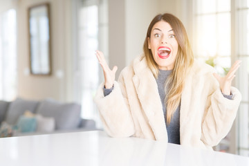 Young beautiful woman wearing winter fur coat at home celebrating crazy and amazed for success with arms raised and open eyes screaming excited. Winner concept