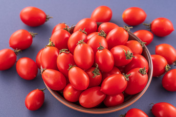 Fresh red cherry tomatoes in a wooden bowl isolated on a blue background, close up, copy space