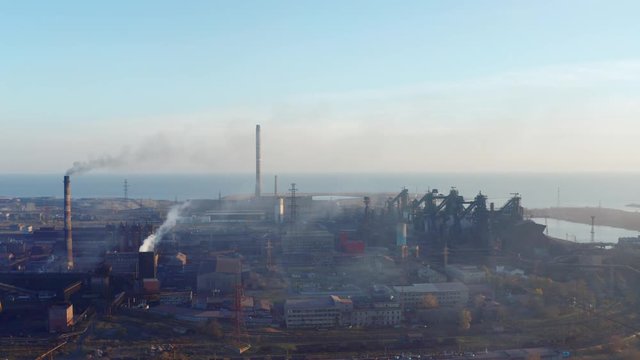 Aerial video. Blast furnaces of a metallurgical plant on the seashore. Pollution of the environment. Evening time