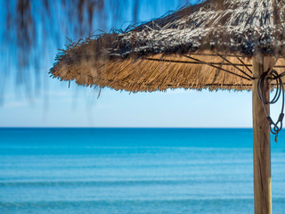 palms leafs straw parasol on the beach with blue sea in the background