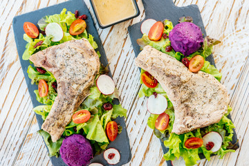 Grilled bbq pork chop meat steak on black plate with vegetable