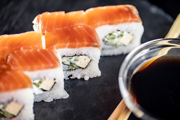 Macro shot of delicious sushi rice rolls on black stone plate with soy sauce and chopsticks