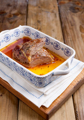 Baked duck fillet in a ceramic baking sheet with patterns on a wooden table. Food for healthy nutrition. Free space for text.