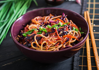 Chinese food. Vegan stir fry noodles with red cabbage and carrot in a bowl on a black wooden background. Asian cuisine meal.