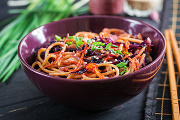 Chinese food. Vegan stir fry noodles with red cabbage and carrot in a bowl on a black wooden background. Asian cuisine meal.