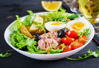 Healthy hearty salad of tuna, green beans, tomatoes, eggs, potatoes, black olives close-up in a bowl on the table. Salad Nicoise. French cuisine.