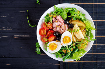 Healthy hearty salad of tuna, green beans, tomatoes, eggs, potatoes, black olives close-up in a...