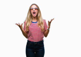 Obraz na płótnie Canvas Young beautiful blonde woman wearing sunglasses over isolated background crazy and mad shouting and yelling with aggressive expression and arms raised. Frustration concept.
