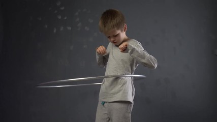 Concept of gymnastics and sports at home. Slender boy in gray tracksuit turns hoop with all his might. Exercise is good for health and development.