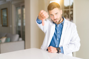 Fototapeta premium Young handsome doctor man at the clinic looking unhappy and angry showing rejection and negative with thumbs down gesture. Bad expression.