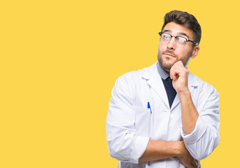 Young handsome man wearing doctor, scientis coat over isolated background with hand on chin thinking about question, pensive expression. Smiling with thoughtful face. Doubt concept.