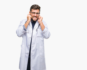 Young handsome doctor man over isolated background covering ears with fingers with annoyed expression for the noise of loud music. Deaf concept.