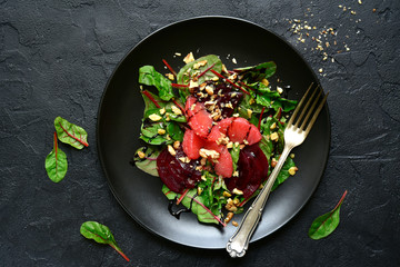Delicious sald with chard leaves, beetroot and grapefruit slices on a black plate.Top view.