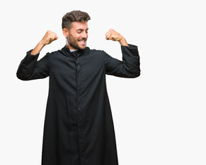 Young catholic christian priest man over isolated background showing arms muscles smiling proud....