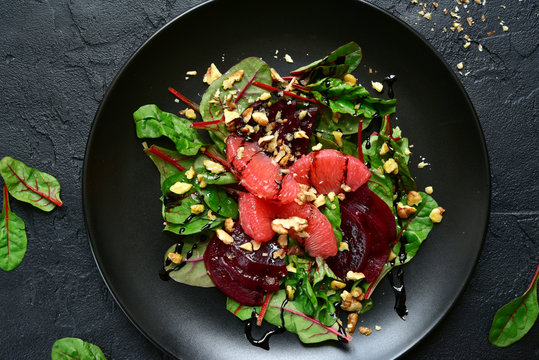 Delicious sald with chard leaves, beetroot and grapefruit slices on a black plate.Top view.