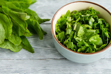 focus on the blue bowl with sliced fresh green sorrel on the wooden table.