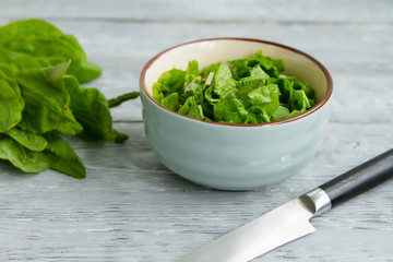 bunch of green sorrel leaves and a bowl of sliced salad on a wooden table