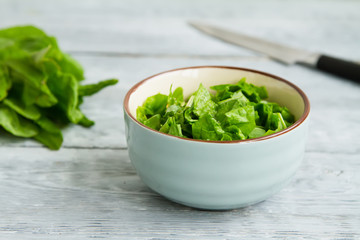 bunch of green sorrel leaves and a bowl of sliced salad on a wooden table