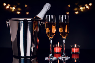 Champagne bottle, two wine glasses and candles with lights