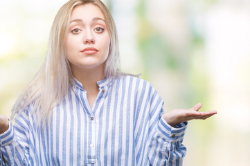 Young blonde woman over isolated background clueless and confused expression with arms and hands raised. Doubt concept.