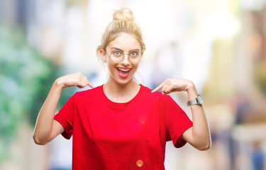 Young beautiful blonde woman wearing red t-shirt and glasses over isolated background looking confident with smile on face, pointing oneself with fingers proud and happy.