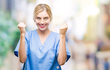 Young beautiful blonde doctor surgeon nurse woman over isolated background celebrating surprised and amazed for success with arms raised and open eyes. Winner concept.