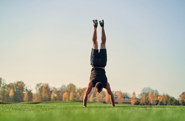 The sportsman standing on hands on the grass