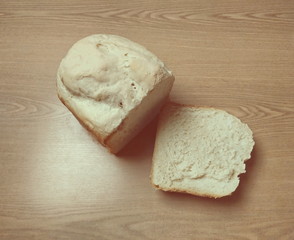Cutted slice and loaf of white quick bread made in bread machine on a wooden table, object in warm colors, space for text