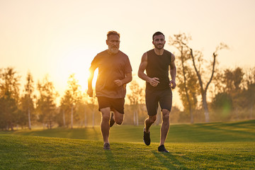 The two sportsmen running on the grass on the sunset background