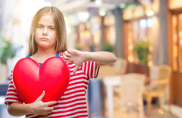 Young beautiful girl holding red heart over isolated background with angry face, negative sign...