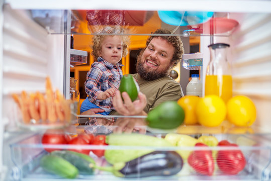 Father and son taking food from fridge late at night. Picture taken from inside of fridge.