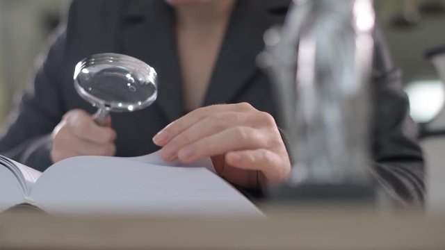 Attorney woman using magnifying glass for law book reading at her office desk, selective focus 