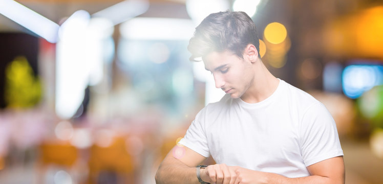 Young handsome man wearing white t-shirt over isolated background Checking the time on wrist watch, relaxed and confident