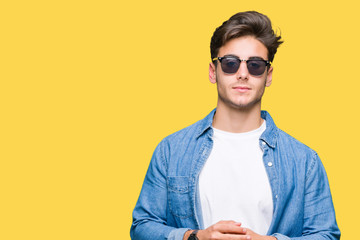 Young handsome man wearing sunglasses over isolated background Hands together and fingers crossed smiling relaxed and cheerful. Success and optimistic