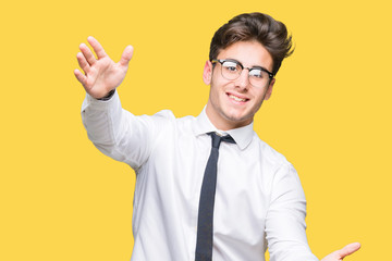 Young business man wearing glasses over isolated background looking at the camera smiling with open arms for hug. Cheerful expression embracing happiness.