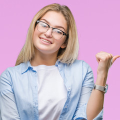 Young caucasian business woman wearing glasses over isolated background smiling with happy face looking and pointing to the side with thumb up.