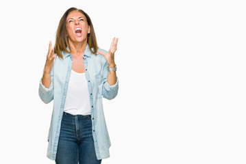 Obraz premium Middle age adult woman wearing casual denim shirt over isolated background crazy and mad shouting and yelling with aggressive expression and arms raised. Frustration concept.