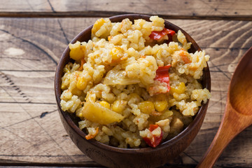 Pilaf with vegetables and chicken in wooden bowl on wooden background.