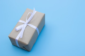 Brown gift box and white bow ribbon on blue background with copy space top view