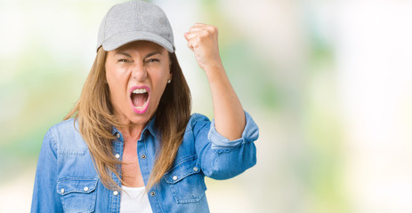 Beautiful middle age woman wearing sport cap over isolated background angry and mad raising fist frustrated and furious while shouting with anger. Rage and aggressive concept.