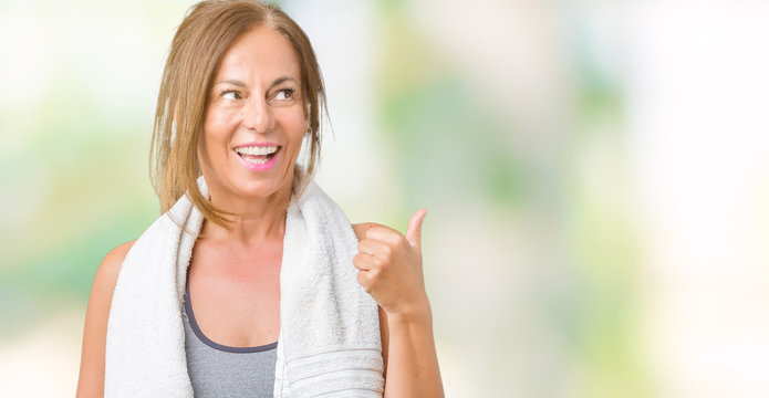 Beautiful middle age woman wearing sport clothes and a towel over isolated background smiling with happy face looking and pointing to the side with thumb up.