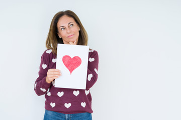 Middle age woman holding card gift with red heart over isolated background serious face thinking about question, very confused idea