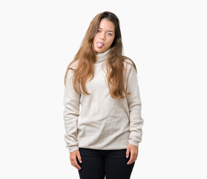 Young beautiful brunette woman wearing turtleneck sweater over isolated background sticking tongue out happy with funny expression. Emotion concept.