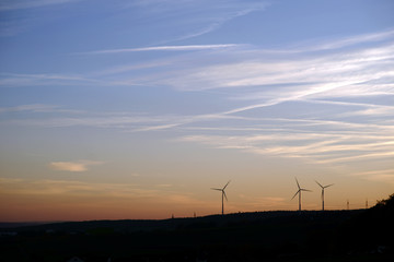 Fototapeta na wymiar Silhouetten von Windrädern vor dem Abendhimmel / Die Silhouetten von Windrädern auf einem bewaldeten Hügel am Abend. ..