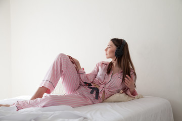 beautiful woman in pink Pajamas listening to music with headphones on the bed