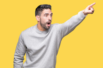 Young handsome man wearing sweatshirt over isolated background Pointing with finger surprised ahead, open mouth amazed expression, something in front